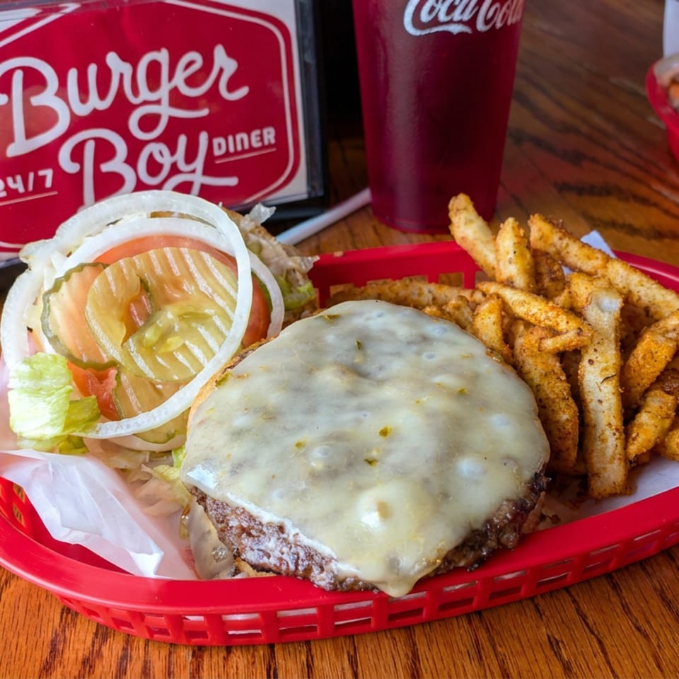 Cheeseburger with lettuce, tomato, onion, and pickles served alongside seasoned fries in a red diner basket.