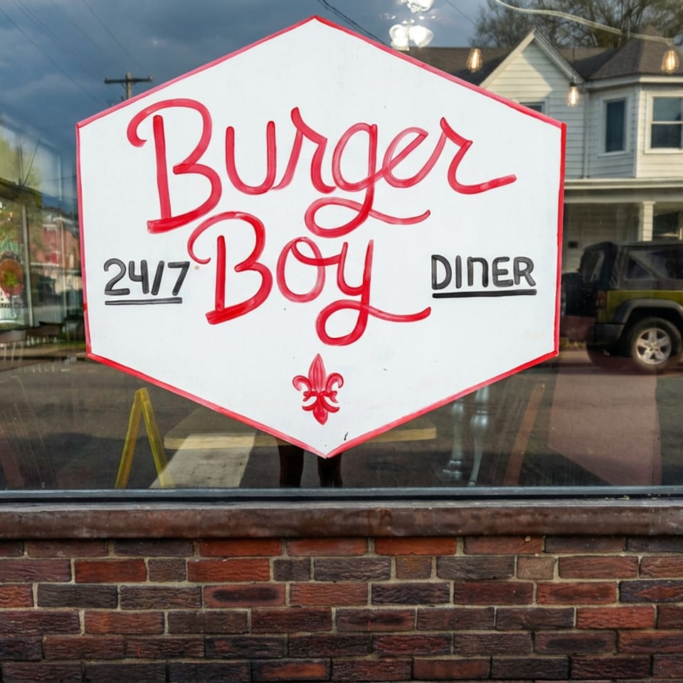 Restaurant window displays a hand-painted Burger Boy Diner sign reading “24/7,” set in a brick exterior.