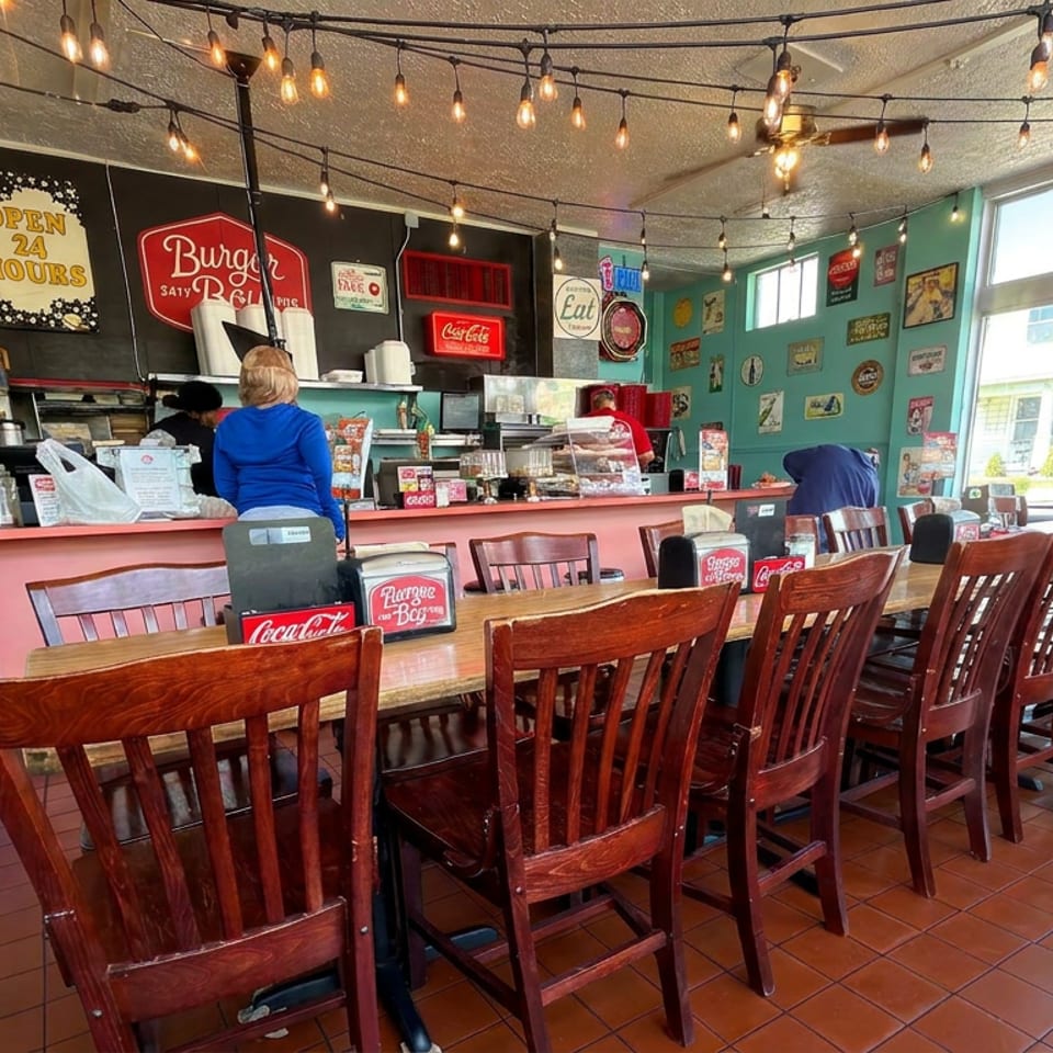 Bright burger restaurant interior with turquoise walls, string lights, wooden tables, counter service, and vintage signs.
